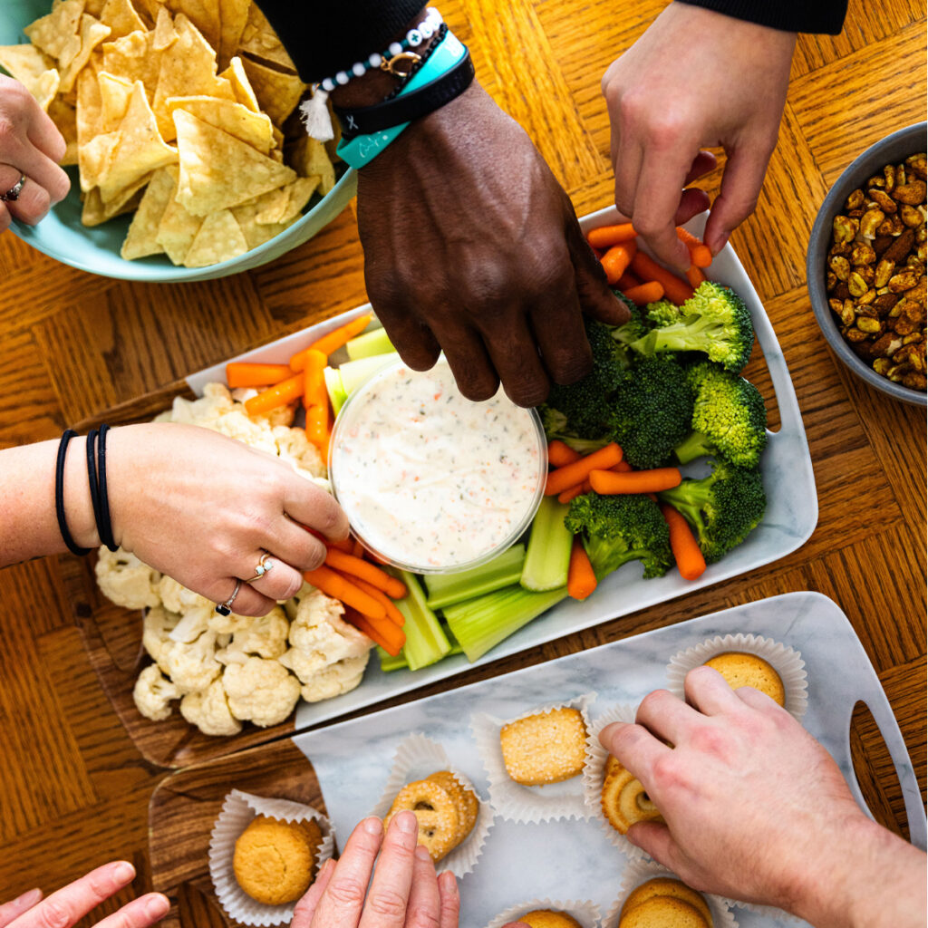 7 peoples' hands reaching in for snacks in the eFIT kitchen lounge